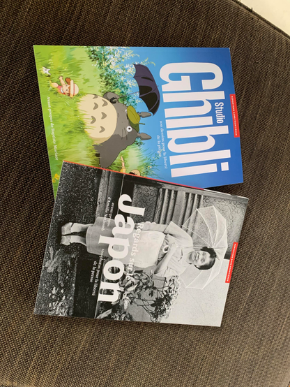 Photo des 2 livres de reporters sans frontières sur le Japon. L’un s’appelle studio Ghibli, 100 dessins pour la liberté de la presse avec le dessin de Totoro avec son parapluie et l’autre s’appelle Regards sur le Japon, 100 photos pour la liberté de la presse avec la photo noir et blanc d’une dame japonaise qui regarde l’objectif, un parapluie à la main. 