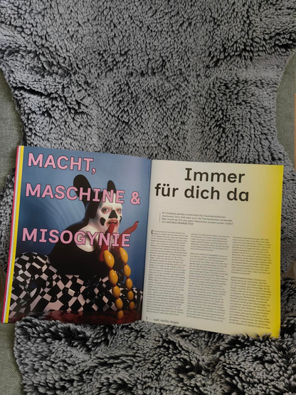 Printausgabe des Anschlaege Magazins. Thema auf der linken Seite "Macht, Maschine, Misogynie" und auf der rechten Seite "Immer für dich da". Ein Artikel über Chatbots.