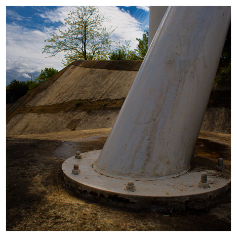 Huge concrete footing ,clamped to concrete base. 
A lone tree in the distance, against a cloud blue sky. 