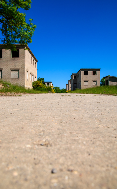 a street with a few small abandoned houses left and right photographed from right above the pavement