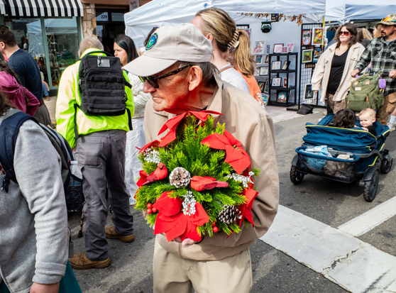 A very old man carrying a colorful autumn door wreath at a fall festival.