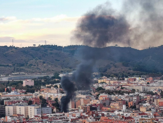 Se ve la ciudad con una columna de humo negro. Las montañas de la sierra de Collserola al fondo y el cielo