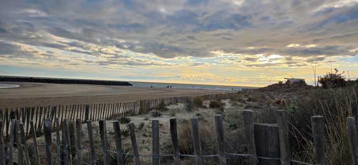 Blick gen Westen
Vorne Holzlatten (verhindern Sandverwehungen) und Dünen
Breiter Sandstrand
Himmel ein gemisch aus grauen Wolken und kleinen sonnigen Abschnitten 