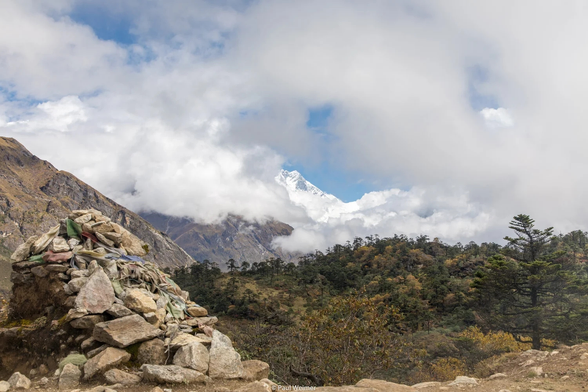 Shot of the mountains mostly covered in clouds, with a cairn with prayer flags in foreground