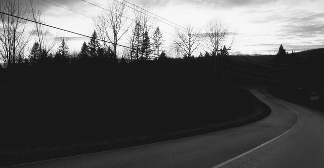 Black and white photograph of a road, curving and descending, with power lines on one side and the forest, still dark as the sky begins to lighten at sunrise.

Photographie noir et blanc d'une route, en courbe et descendante, avec des lignes électriques sur un côté et la forêt, encore sombre alors que le ciel commence à s'éclaircir au lever du soleil.