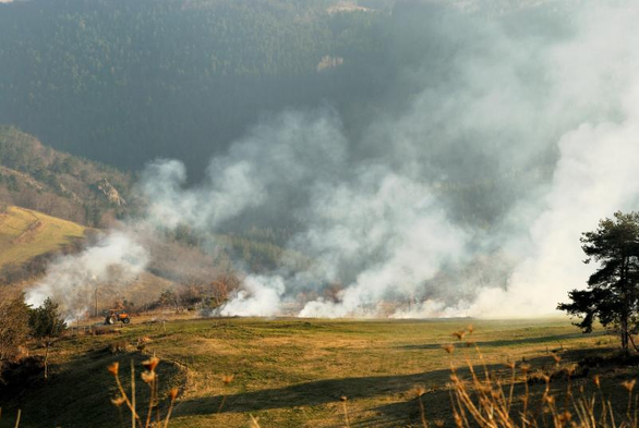 Une image au format paysage montre des champs en automne,  descendant en terrasse vers un fond de vallée et le versant opposé de la colline. L'herbe à déjà jauni, oscillant du vert bronze à l'orangé. Trois feux destinés à brûler des branchages sont alignés au tiers inférieur de l'image et la fumée masque partiellement le relief à droite.