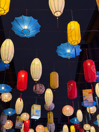 Colorful lanterns and parasol-shaped lights hang above a street at night in Xi’an, creating a festive and vibrant atmosphere against the dark sky.