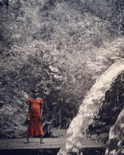 Une jeune fille habillée d’une jupe et d’un t-shirt rouge près d’une chute d’eau