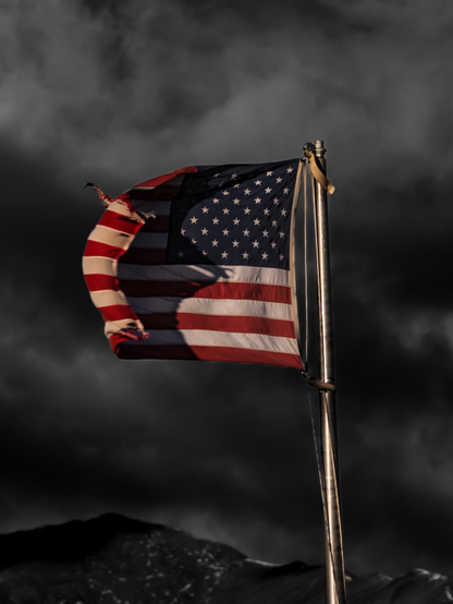 A tattered USA flag whips in the wind in front of ominous dark skies
