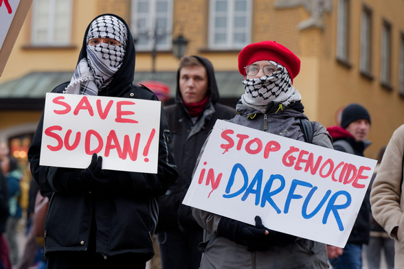 Two people with faces covered with keffiyehs, holding placards saying "Sva Sudan!" and "Stop genocide in Darfur"