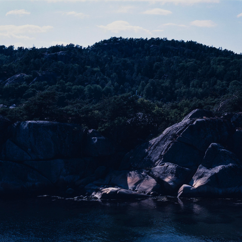 Coastal landscape with cliffs, big rocks and a forest clad hill. Dear sea water, light clouds in the sky.