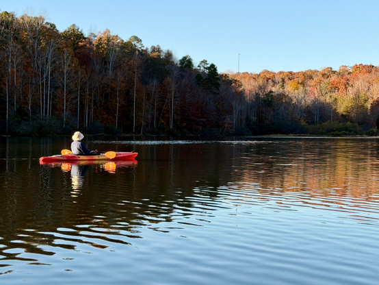 Paddler in the shadow of a hillside in a lake in the foothills. Fall colors. 