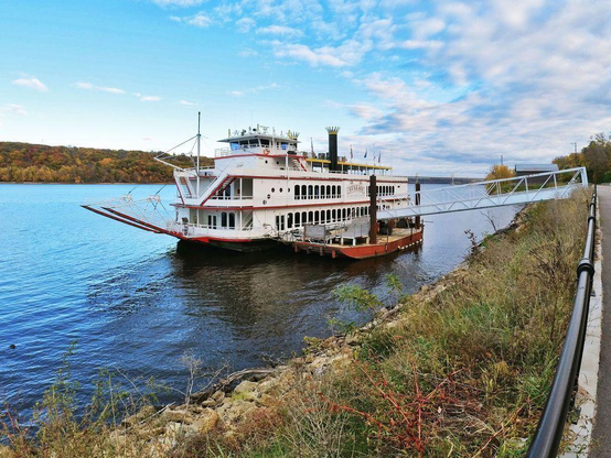 One of a series of scenes from the Stillwater, Minn., riverfront area, featuring a bridge crossing the Mississippi River, riverboats docked at a marina, and rusty chains connecting concrete pillars along the shoreline’s walkway.
