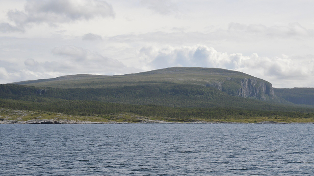 A photo of water leading to a mountainous cliff. The sky is filled with clouds.