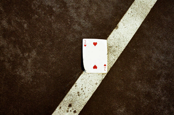 A deuce of hearts laying on a white painted line on asphalt.