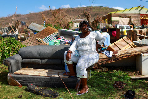 A woman sits on a sofa in front of the remains of her house.