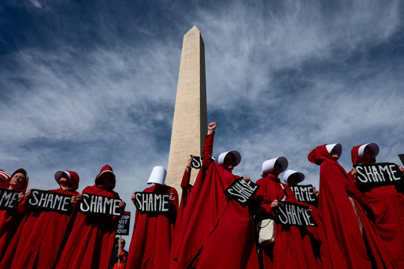 Demonstrators dressed as handmaidens from "The Handmaid's Tale" take part in an anti-Trump protest marking one year since the re-election of President Trump, at the Washington Monument in #Washington, holding placards with the word 'SHAME'