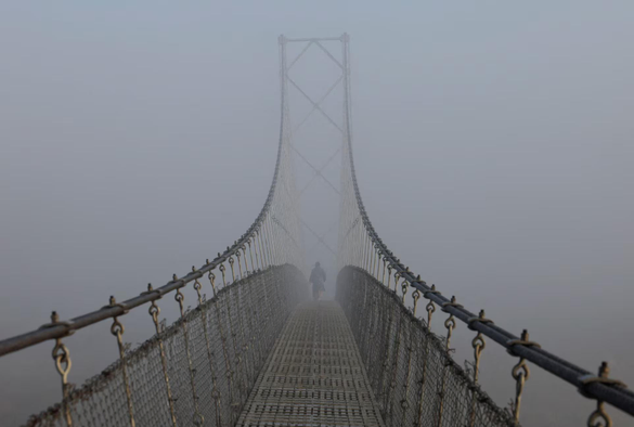 A woman walks on a suspension bridge, during a foggy morning.