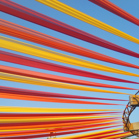 Colorful fabric strips in shades of red, orange, and yellow stretch across a clear blue sky