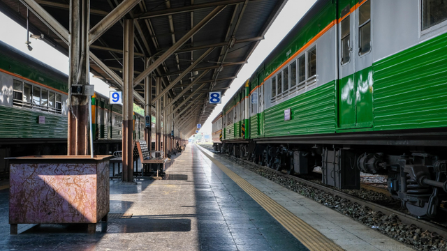 color photo of a stationary passenger train (in green & white paint) at an empty metal roofed platform