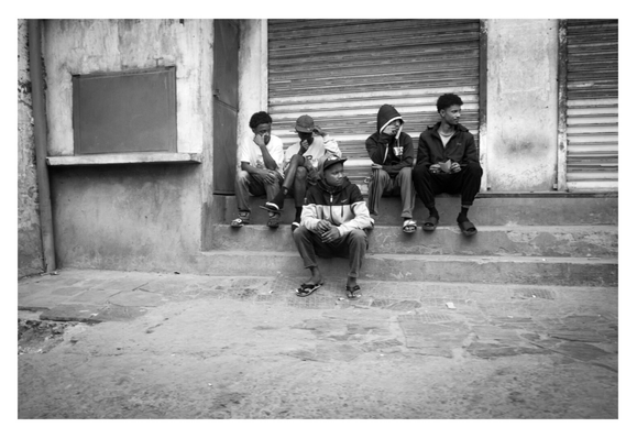 Des personnes assises sur un escalier, devant un magasin fermé.