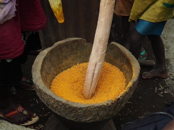 Enfants dont on voit juste les jambes, autour d’un grand mortier et pillon 