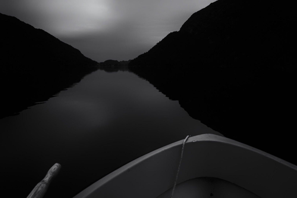 Black and white photography of boat and lake and hillsides.