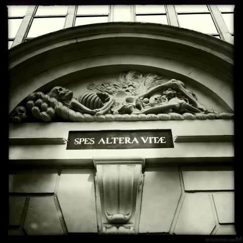 Moody monoschrome photo of an old ornament on an Amsterdam building, featuring a sculpture of a lying skeleton. Underneath is the text "Spes Altera Vitae".