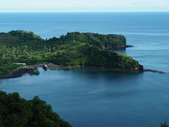 Paysage de bord de mer, un bras de terre s’avance dans la mer très calme. Un bateau en bord de plage