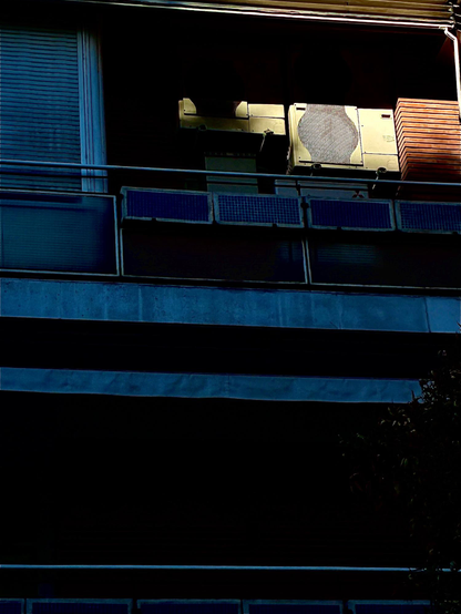 Terraza en las sombras. La parte superior derecha, donde hay un aire acondicionado suspendido de la pared, iluminada por el sol. Las sombras azules, el sol amarillo y naranja.
