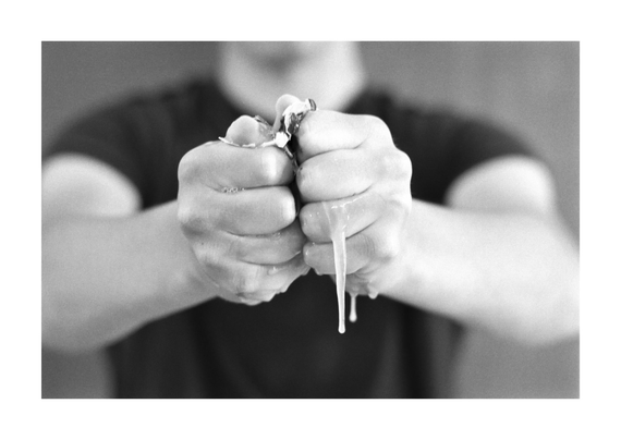 Unas manos con los puños cerrados rompen un huevo, mientras se esparcen sus restos entre los dedos. Foto en blanco y negro.