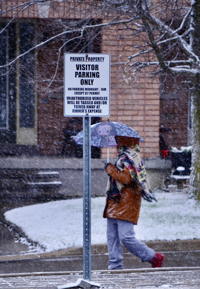 A neighbour under an umbrella walking in a light snowfall through a residential street.
