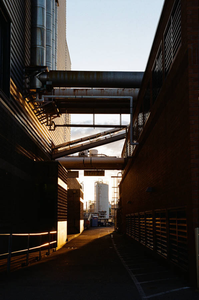 A narrow alleyway between corrugated metal buildings. Ducts and pipes run between the buildings.