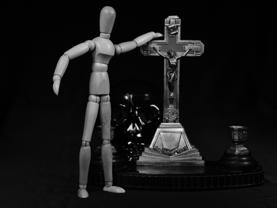 Mannequin de bois posant la main sur un crucifix en arrière plan une tête de mort.