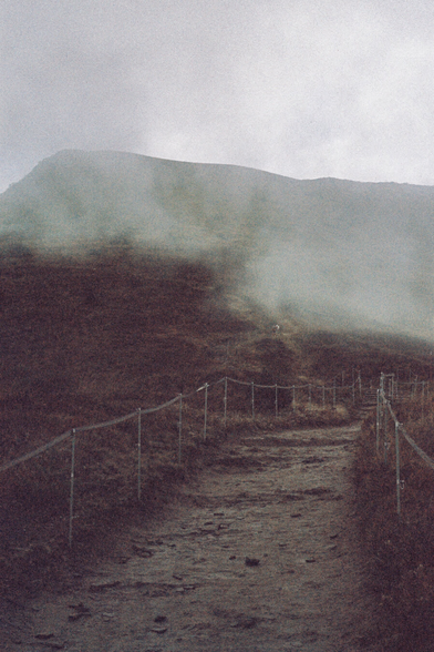 A marked path in the mountains, a cross can be seen at the top, it is raining, foggy and muddy.