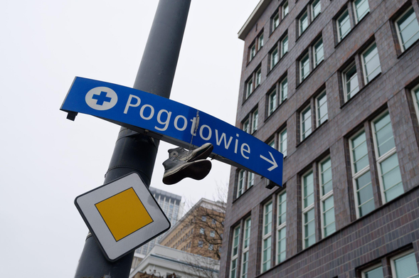 A pair of old Converse shoes hung on a sign showing directions to the emergency service nearby. Building of Ministry of Infrastructure and Construction can be seen in the background.