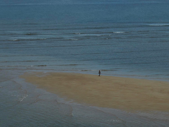 Silhouette d’un enfant marchant sur une bande de sable entourée par la mer.
