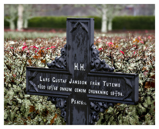 En liggande bild på en gravmarkering i form av ett kors i svart metall med texten ”H.H. Lars Gustaf Jansson från Tutemo. Född 1868 omkom genom drunkning 1894. Ps. 476:1.”

Bakom är en grågrön häck med några röda löv. I bakgrunden står några björkar framför en grön häck.