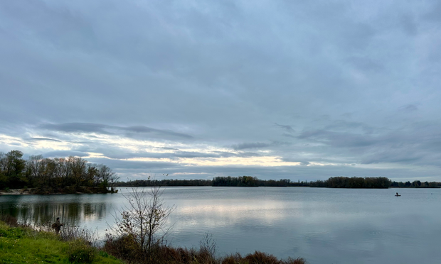 Un lac au crépuscule. On devine un pêcheur sur la berge. Une percée de lumière à travers les nuages éclaire la scène. 