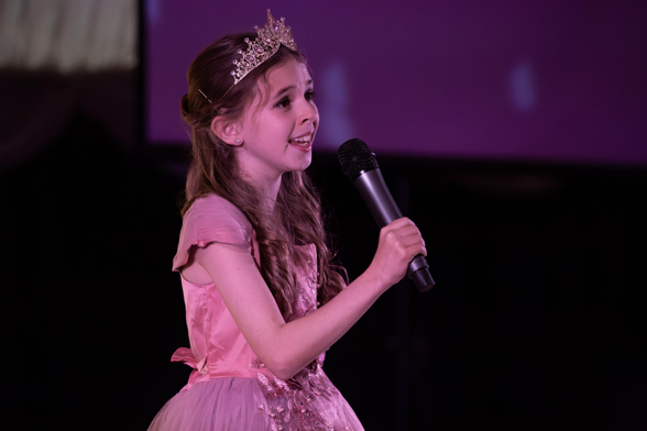 Young girl, in a pink dress singing on stage