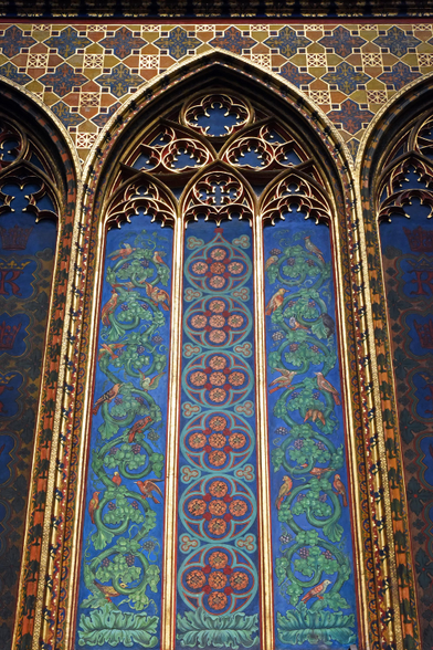 Color photo of an interior wall which features a series of blind arches richly decorated with natural and geometric designs executed primarily in shades of blue, green, and orange. Each of the larger arches contains a trio of smaller (narrower) arches divided by gilded piers. Gilded tracery fills the upper portion of each of the large and small arches.