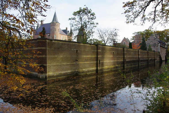 Breed zicht op de gebouwen van kasteel Heeswijk, met de muren en de gracht daaromheen