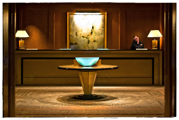 The Four Seasons Hotel. 
Monday, April 12th, 2012, 2:47 p.m.

This is the exact moment when Bob discovered shooting at f/1.4 would not kill him... and he promised to do it again in another decade or two.

Okay seriously, this is a photograph of a beautifully lit, anally minimalistic, very upscale, uber-tasteful hotel lobby in downtown San Francisco.

Picture - in sharp focus - a post-modern, round table sitting in the center of a rust and camel colored carpet. On top of the table sits a cyan glass bowl, illuminated with heavenly light from above. In softer focus behind the table: a sleek, wooden reception desk that stretches the width of the photo. Add two handsome table lamps, a wood paneled wall, a large, unoffensive abstract painting, designer spot lighting, and a smartly dressed receptionist who is cradling a phone with her neck and shoulder. 

It's a wonderful scene. Handsome. Painterly. New money-ish.

As my husband Chris would say: just put a little pony on it and Ralph Lauren would claim it as his.