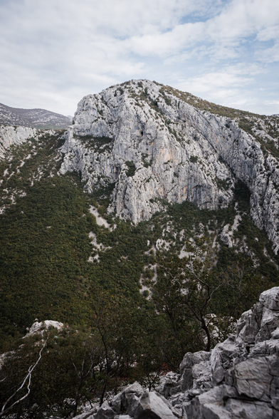 A rocky limestone mountain formation, with a precipice and trees at the bottom of the frame.