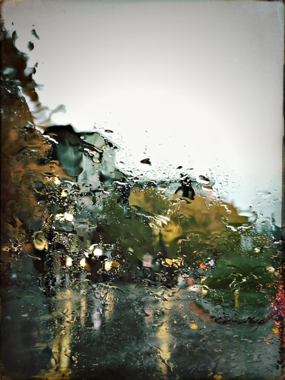 Color photo of rainy, blurred out orange trees, car heads lights and a wet road and buildings through a window.