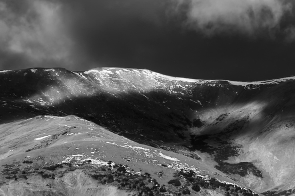 A mountain range under heavy clouds, with shadows covering parts