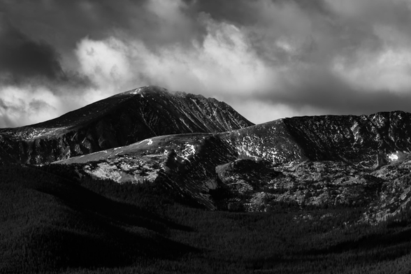 Snow dusted mountains under heavy clouds with the shadows from the clouds dotting the landscape