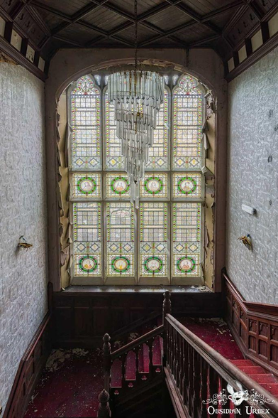 large stained glass window overlooking wooden stairs, with red runner. a huge crystal chandelier hangs above the stairs