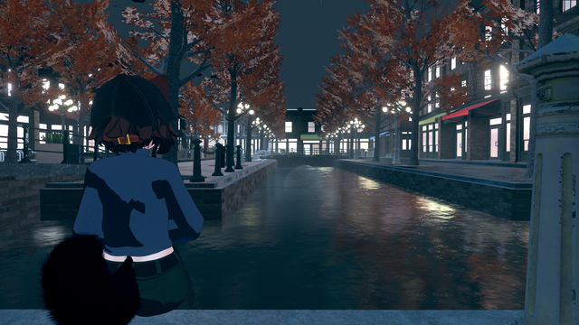 A stylized 3D scene shows a character with short brown hair, wearing a dark cap and blue sweater, standing beside a canal at night. The canal is lined with autumn trees and glowing streetlights that reflect off the water. Brick buildings with bright windows and colorful awnings line both sides of the canal, creating a calm, urban evening atmosphere.