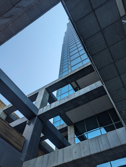 Looking up through the structure of the building at the corner of North St Paul St and Ross Ave in downtown Dallas, TX.

Square geometric latticework of concrete with some wood accents, framed vertically and offset at an angle, with the glass skyscraper part of the building partially visible through the latticework.